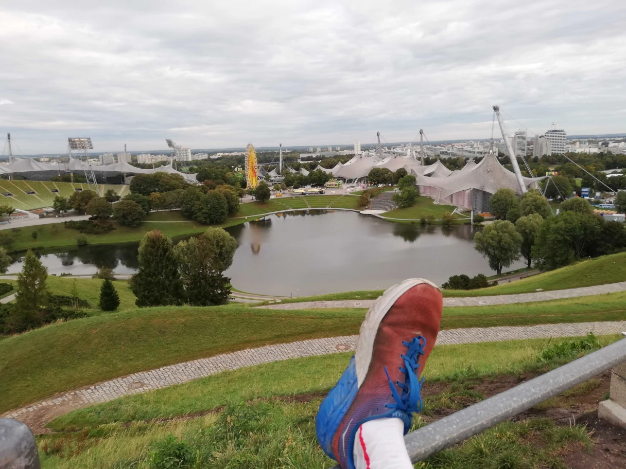 Olympiapark, Mann hält seinen Joggingschuh auf einer Stange in die Höhe, Blick über den Olympiapark München