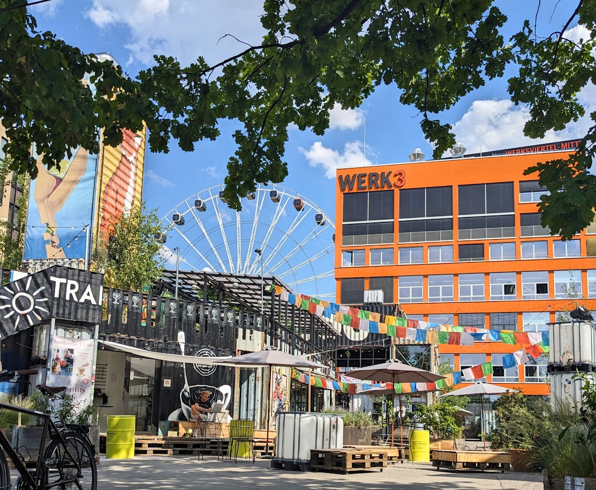 Werksviertel Mitte, Draußenbereich mit bunter Deko und Bars/Restaurants. Im Hintergrund das Riesenrad Umadum