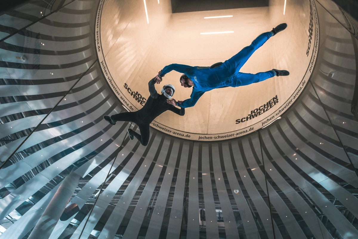 Two young men float holding hands in the wind tunnel