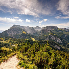 Blick auf die Berge in Bayern mit Weitwinkel fotografiert. Es ist Sommer, es sind ein paar Wolken am Himmel aber die Sonne scheint und es ist viel grün zu sehen