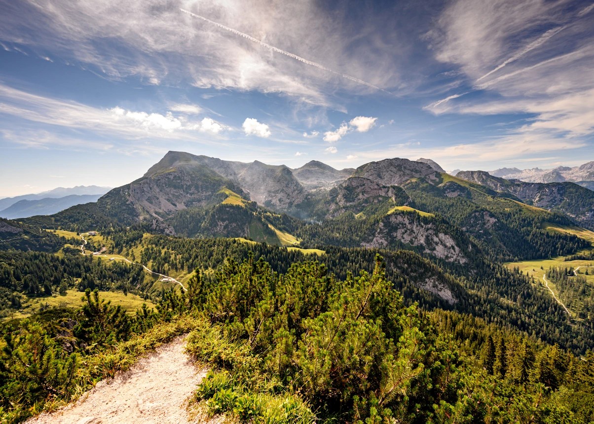 Blick auf die Berge in Bayern mit Weitwinkel fotografiert. Es ist Sommer, es sind ein paar Wolken am Himmel aber die Sonne scheint und es ist viel grün zu sehen
