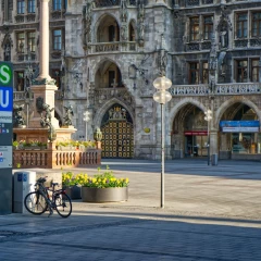 Ein Teil des Marienplatzes. Sie Sonne scheint, es ist kein Mensch zu sehen, links ist der Eingang zum U- und S-Bahnhof. Im Hintergrund ist das neue Rathaus