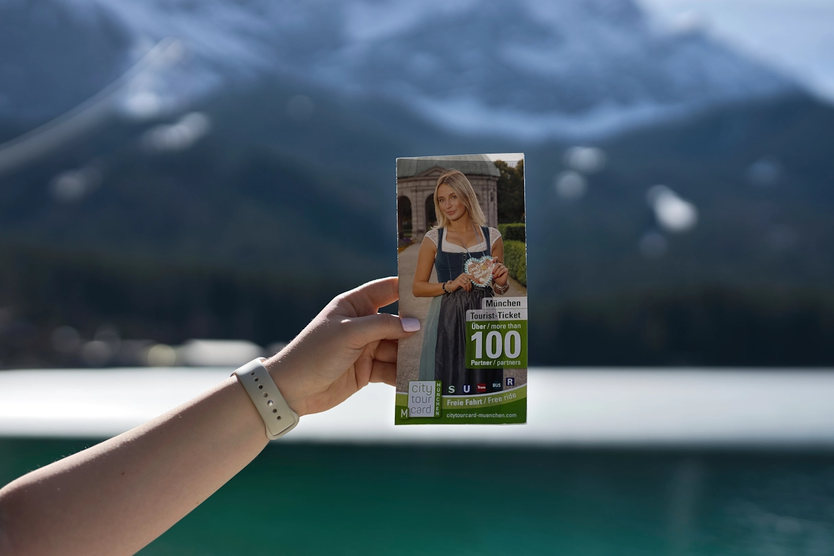 CityTourCard München Flyer, eine Hand hält den Flyer, im Hintergrund ist der vereiste Eibsee zu sehen