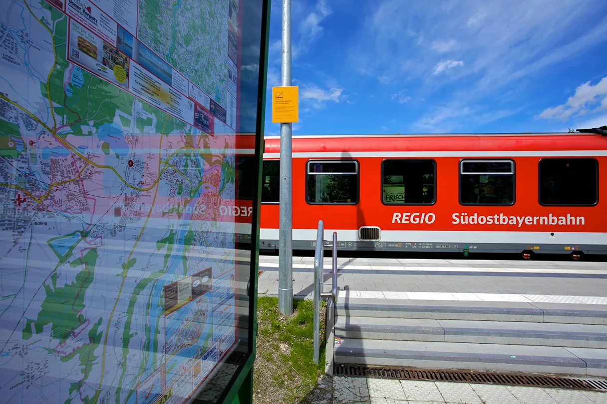 MVV, roter Regionalzug fährt am Bahnhof ein, links ist eine Karte von München hinter einer Glasscheibe