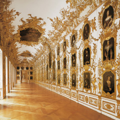 Die Ahnengalerie in der Münchner Residenz. Ein langer Flur, an den Wänden hängen viele Portraits von Adligen. Wände und Decke sind mit einem Goldmuster verziert