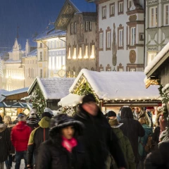 Bad Tölz Christmas market in the Marktstraße. Lots of people are walking around, the stalls are covered in snow