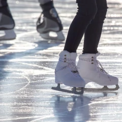 zwei Personen fahren mit Schlittschuhen über eine Eisfläche. Man sieht nur die Füße bzw. die Beine.