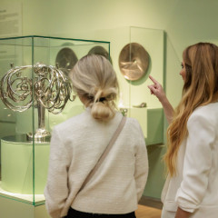 Zwei Besucherinnen in der Kunsthalle München bei der Ausstellung Jugendstil Made in Munich. Sie schauen sich einen großen und silbernen Kerzenständer an