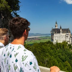 Zwei junge Männer blicken von weitem auf das Schloss Neuschwanstein