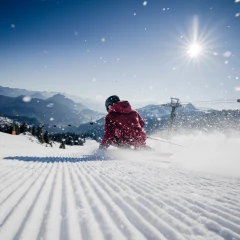 Skigebiet Sudelfeld, ein Skifahrer rast den Berg hinunter. Die Sonne scheint und man erkennt Berge im Hintergrund