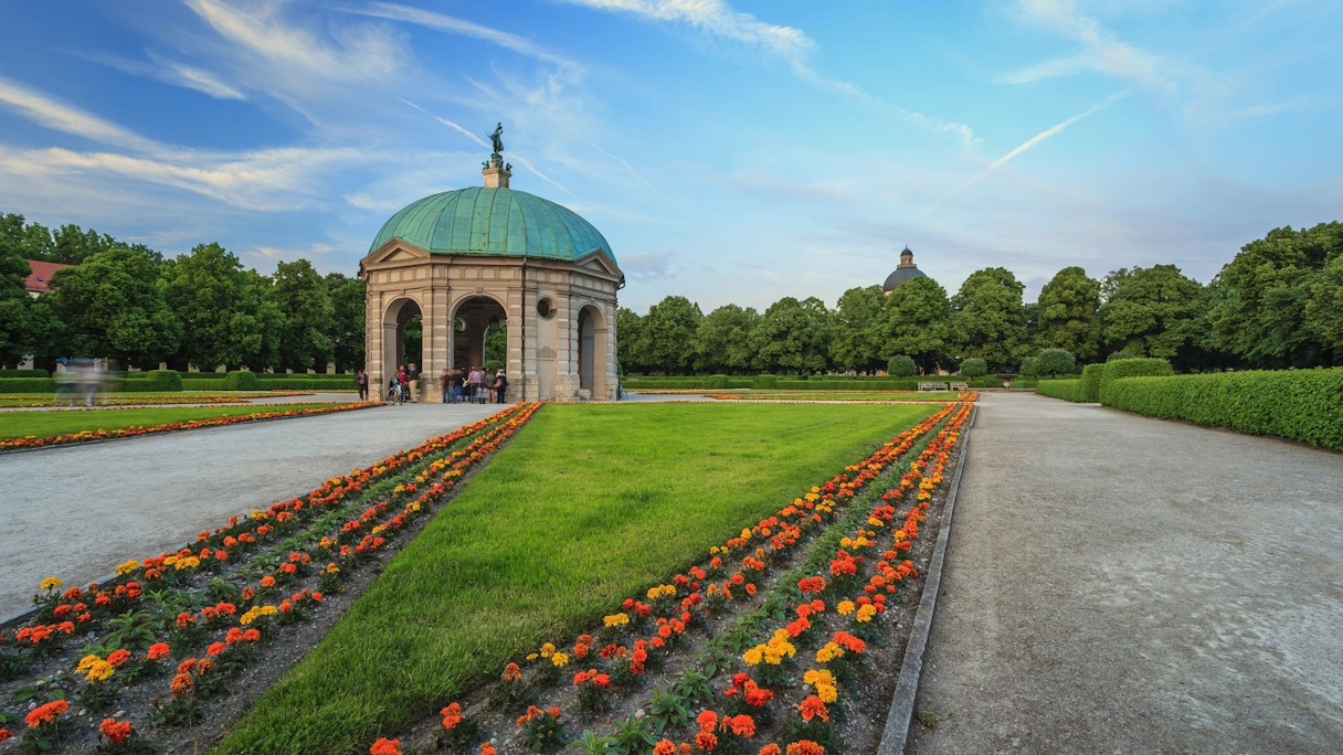 Der Hofgarten in München. In der Mitte ist der bekannte Pavillon zu sehen, drun herum sind grüner Rasen und bunte Blumen zu sehen