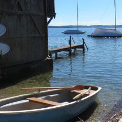Starnberger See bei gutem Wetter. Holzhütte und Holzsteg, daneben sind Boote auf dem Wasser
