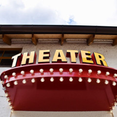 The entrance to the Hoftheater Munich. Above the door is a large sign with the word “THEATER.” Below it are small lamps or light bulbs that light up in the evening.