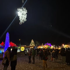 Abends auf dem Tollwood Winterfestival. Man sieht viele Menschen und bunte Lichter glitzern