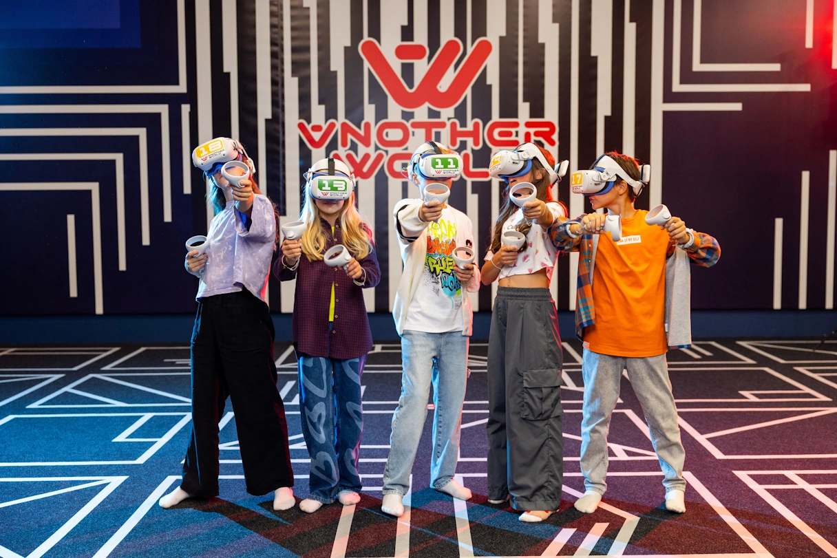 5 Kinder bei Another World Munich - eine Virtual Reality Arena. Die Kinder haben VR Brillen auf und halten Controller in der Hand