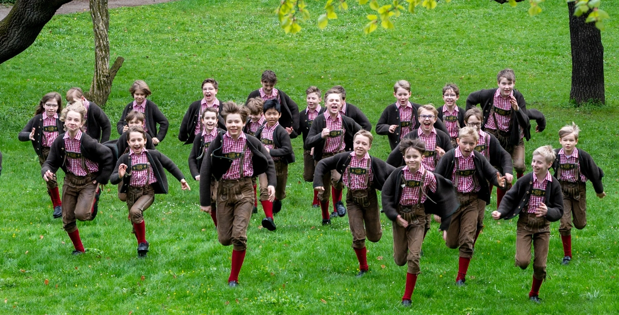 jüngere Mitglieder des tölzer Knabenchor rennen in Tracht gekleidet über eine WIese