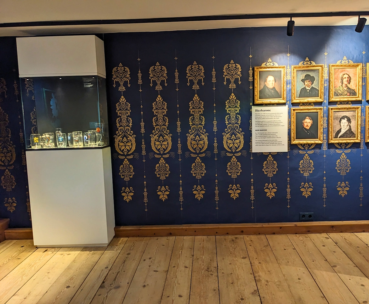 Bier & Oktoberfestmuseum Ausstellung, links verschiedene Bierkrüge und rechts Gemälde von damaligen Bierbaronen, darunter eine Frau