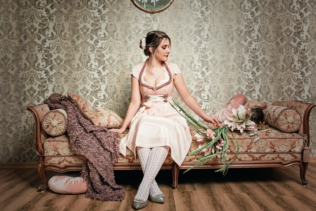 junge Frau mit rosa Dirndl auf einem Sofa im altmodischen Look