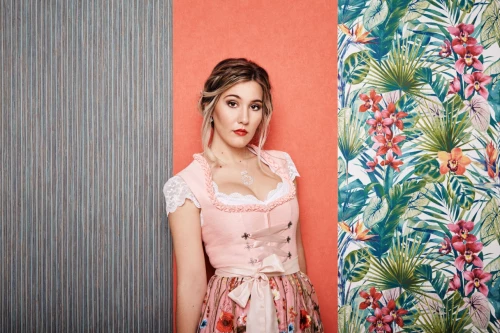 Young woman with pink floral dirndl in front of flower wall