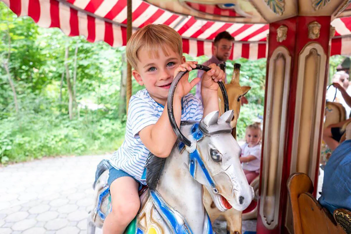 Märchenwald München, Junge sitzt auf einem Karusselpferd und guckt in die Kamera
