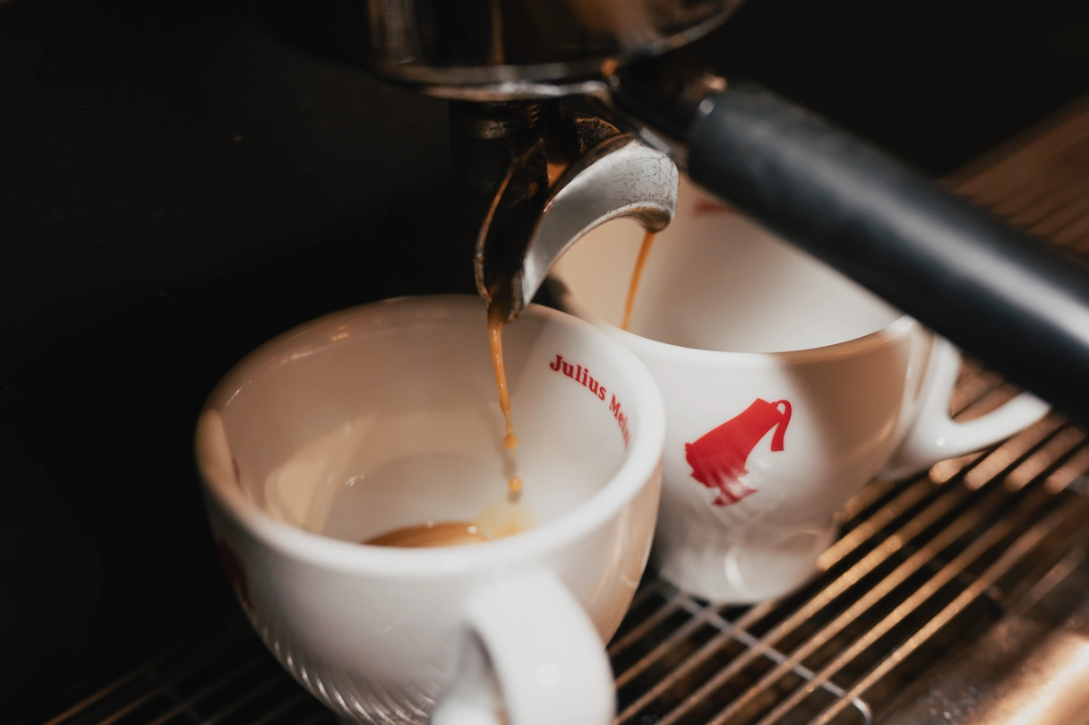 Two coffee cups under a coffee machine. The coffee is pouring into the cups.