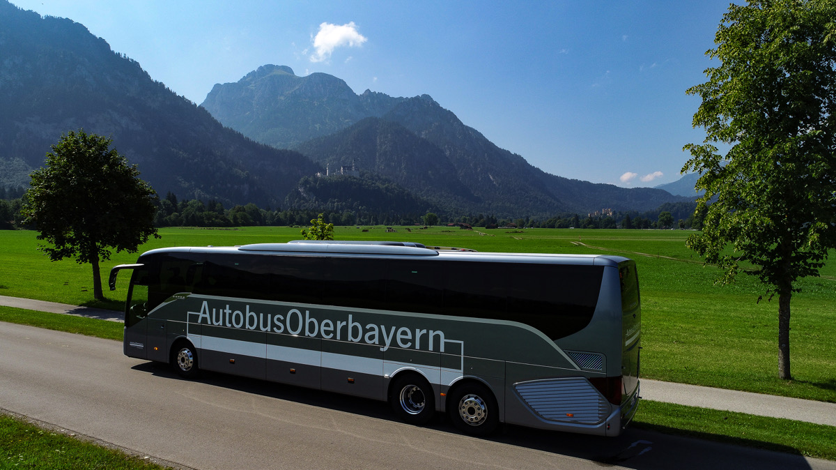 Gray Line Bus in Oberbayern mit grüner Wiese und Bergen im Hintergund