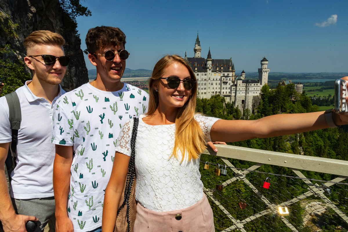 3 junge Touristen in Neuschwanenstein machen ein Foto mit dem Schloss im Hintergrund
