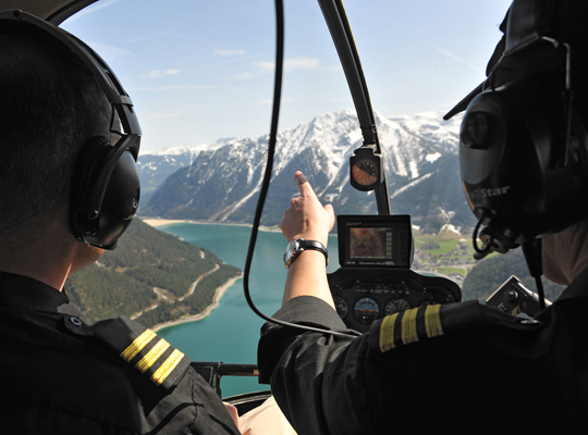 Pilot und Copilot im Helikopter mit Ausblick auf See und Berge