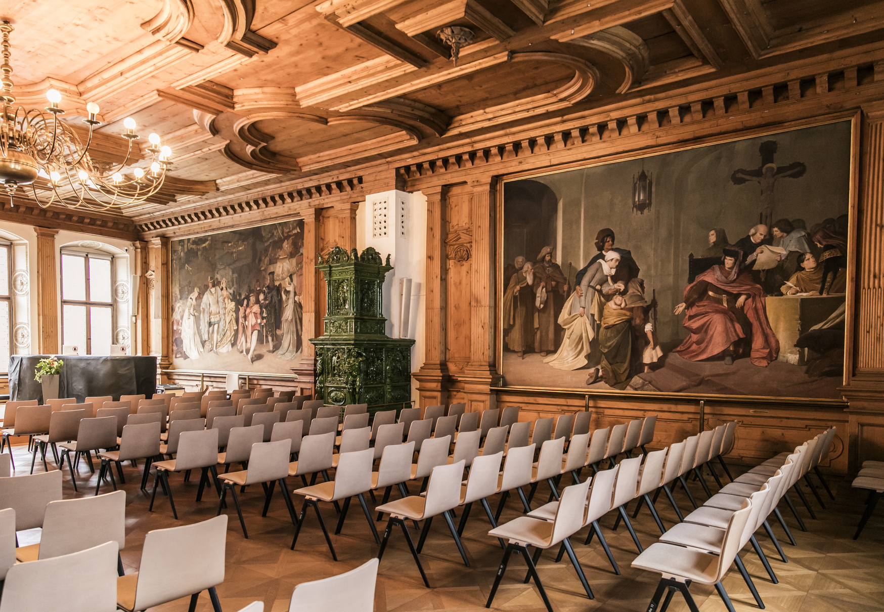 Ballroom in the Historic City Hall in Landsberg. Several rows of chairs, large historic paintings on the walls, and wooden decorations on the ceiling