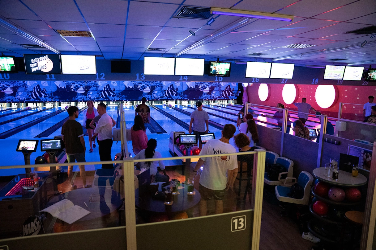 Menschen spielen auf mehreren Bahnen Bowling, bei buntem Licht