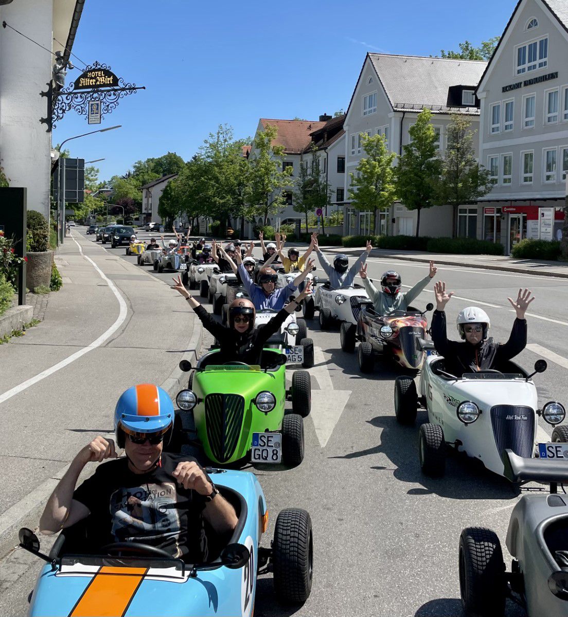 Hot rod drivers in go karts driving in a row on the streets of Munich, passing the old landlord