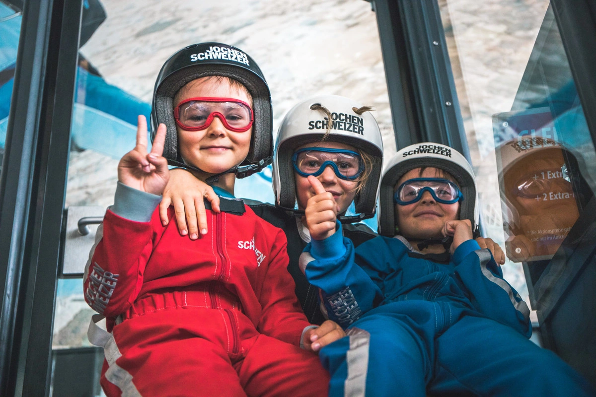 Drei Kinder die ihre Ausrüstung zum Bodyflying tragen und fröhlich in die Kamera lächeln