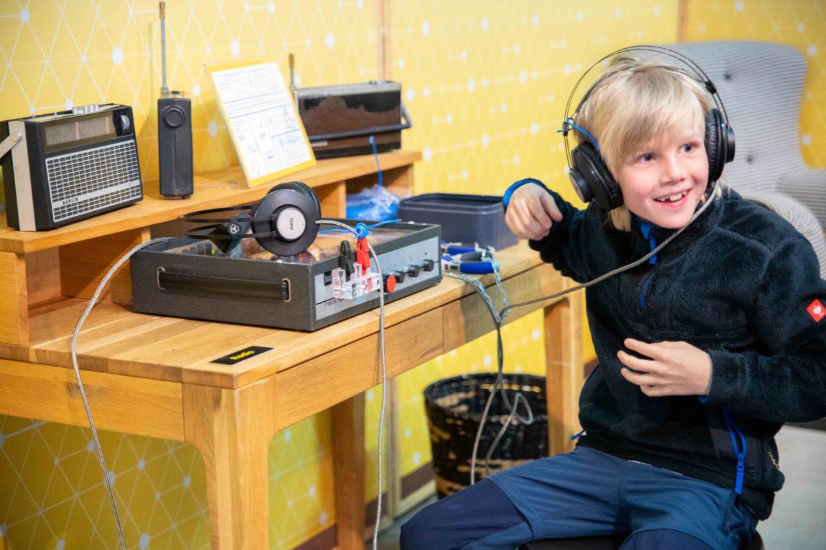 Kleiner Junge im Kindermuseum an einer Musik- und Radiostation mit Kopfhörern auf
