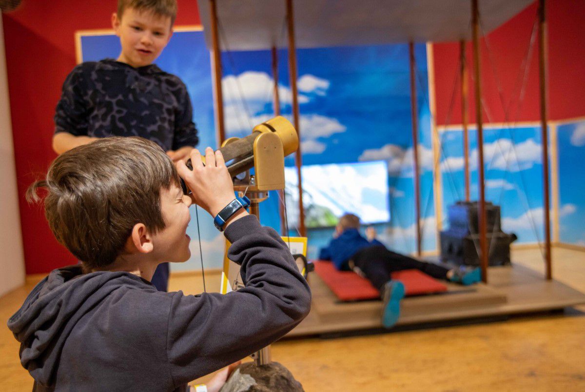 Two boys at a sampling station in the Children's Museum, one looking through binoculars