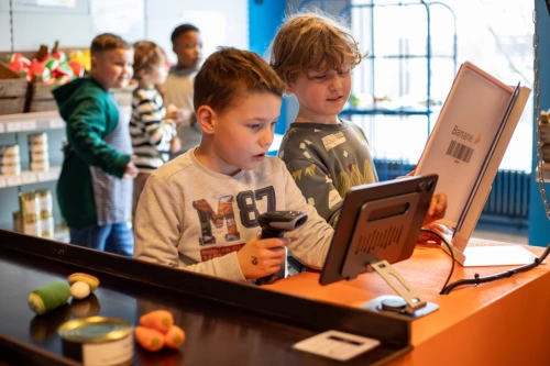 Mitmachausstellung im Kindermuseum. Die Kinder stehen an einer spielrisch nachgestalteten Supermarktkasse und scannen ihre Artikel