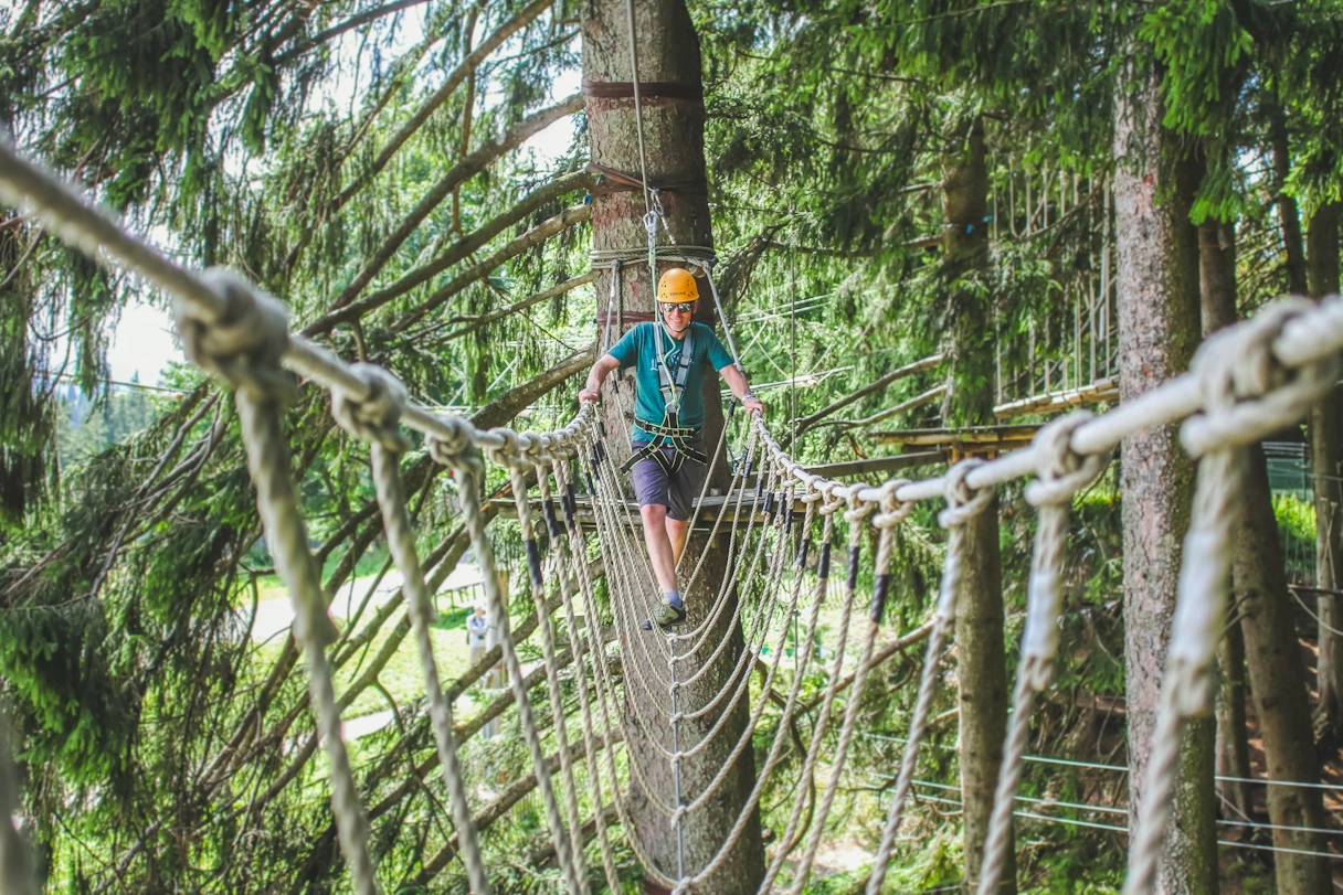 A man walks across a rope bridge high above the ground in the climbing forest