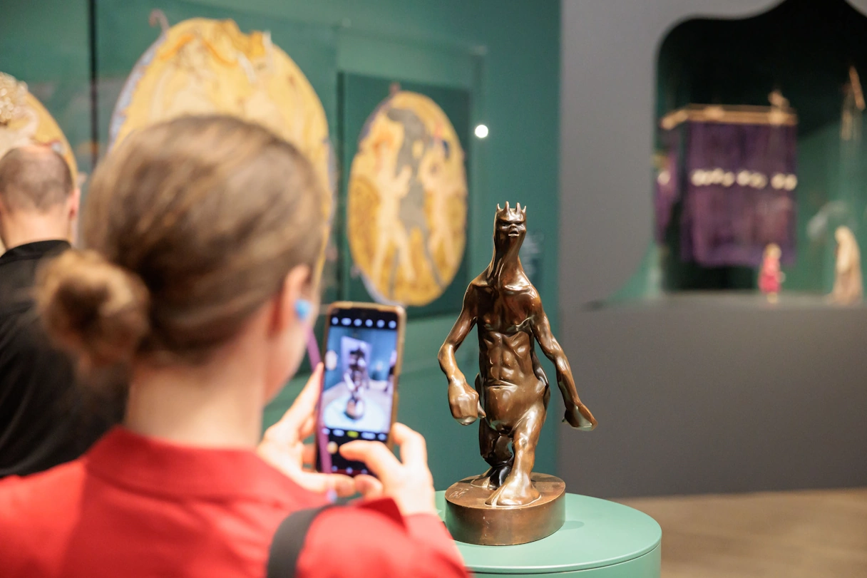 Young woman photographs a small brown statue in the Kunsthalle Munich