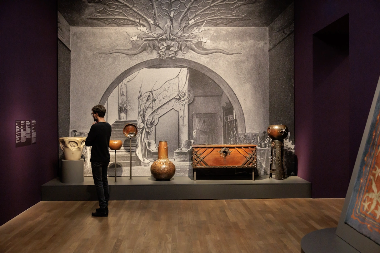 Exhibition room in the Kunsthalle Munich. On the wall is a black and white drawing depicting the interior of a house. In front of it is real wooden furniture