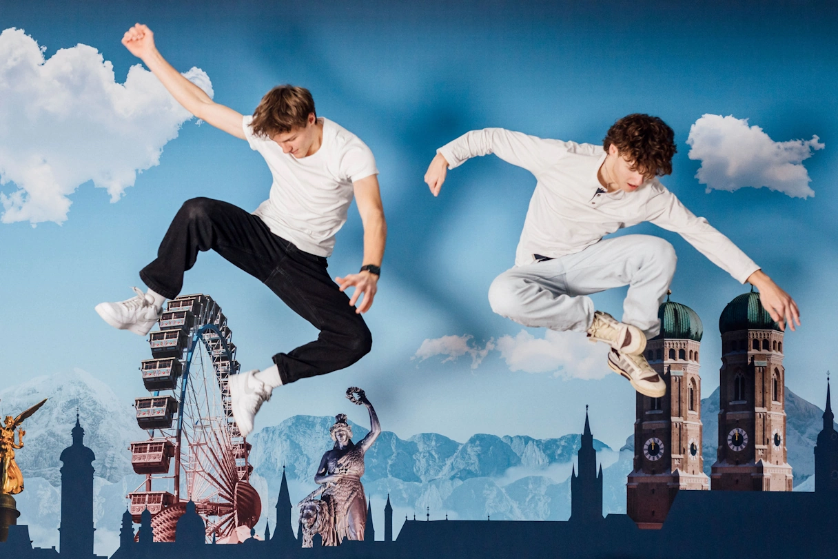 Zwei Jungs in einer Sprungpose vor einer Wand mit Motiven von Münchner Sehenswürdigkeiten
