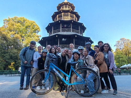 Der Chinesische Turm im Englischen Garten München. Davor steht eine Gruppe, die eine Fahrradtour durch München macht. Im Vordergrund steht das gelihene Fahrrad von Mike's Bike Tours