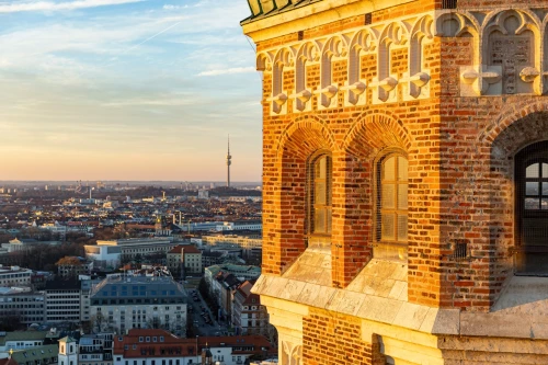 Blick vom Südturm der Frauenkirche München über die Stadt und auf den Nordturm. Weit im HIntergrund am Horizont sieht man den Olympiaturm