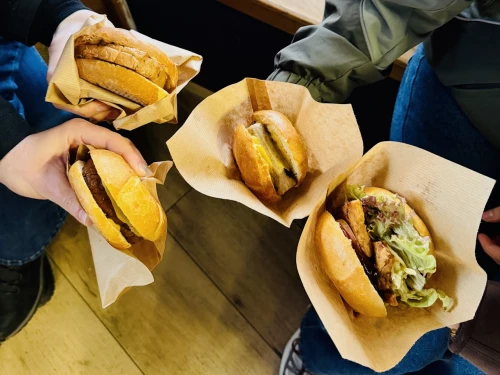 Vier vegane Burger nebeneinander gehalten. Die Burger sind in braunem Papier eingewickelt.
