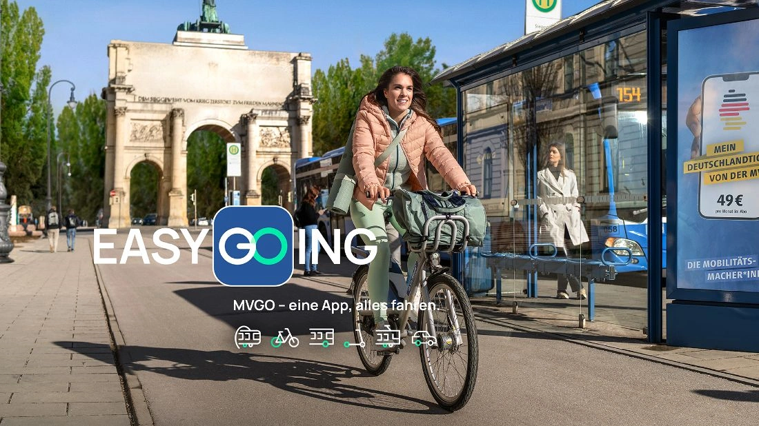 Frau fährt mit einem MVG Rad an einer Bushaltestelle vorbei, im Hintergrund sieht man das Siegestor