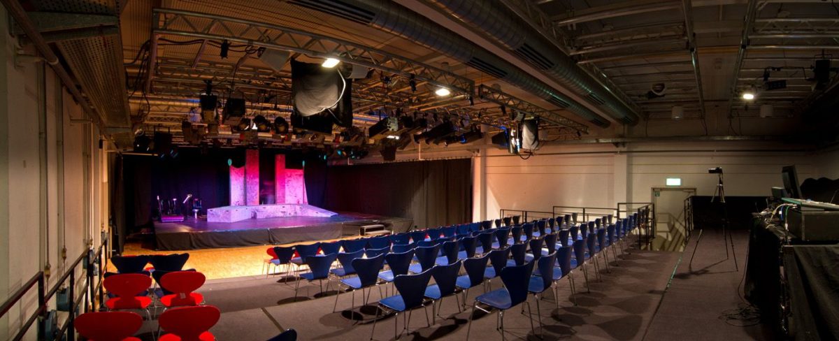 Theater- und Konzertraum mit beleuchteter Bühne und leeren Sitzplätzen