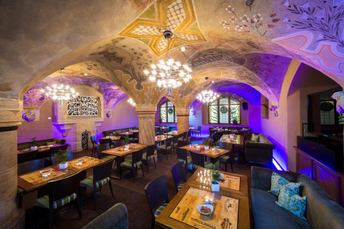Ratskeller München, Kellergewölbe, mit lila Lichtakzenten ausgeleuchtet, verschiedene Tische stehen für die Gäste bereit