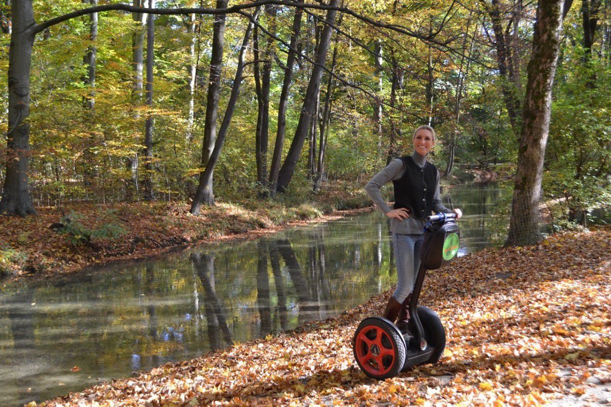 Seg to rent München, Tourist fährt auf einem Segway durch einen Wald und stoppt an einem kleinen Fluss