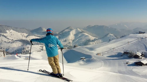 Young man on skis stands on a mountain in Sudelfeld. Snow-covered mountains can be seen in the background
