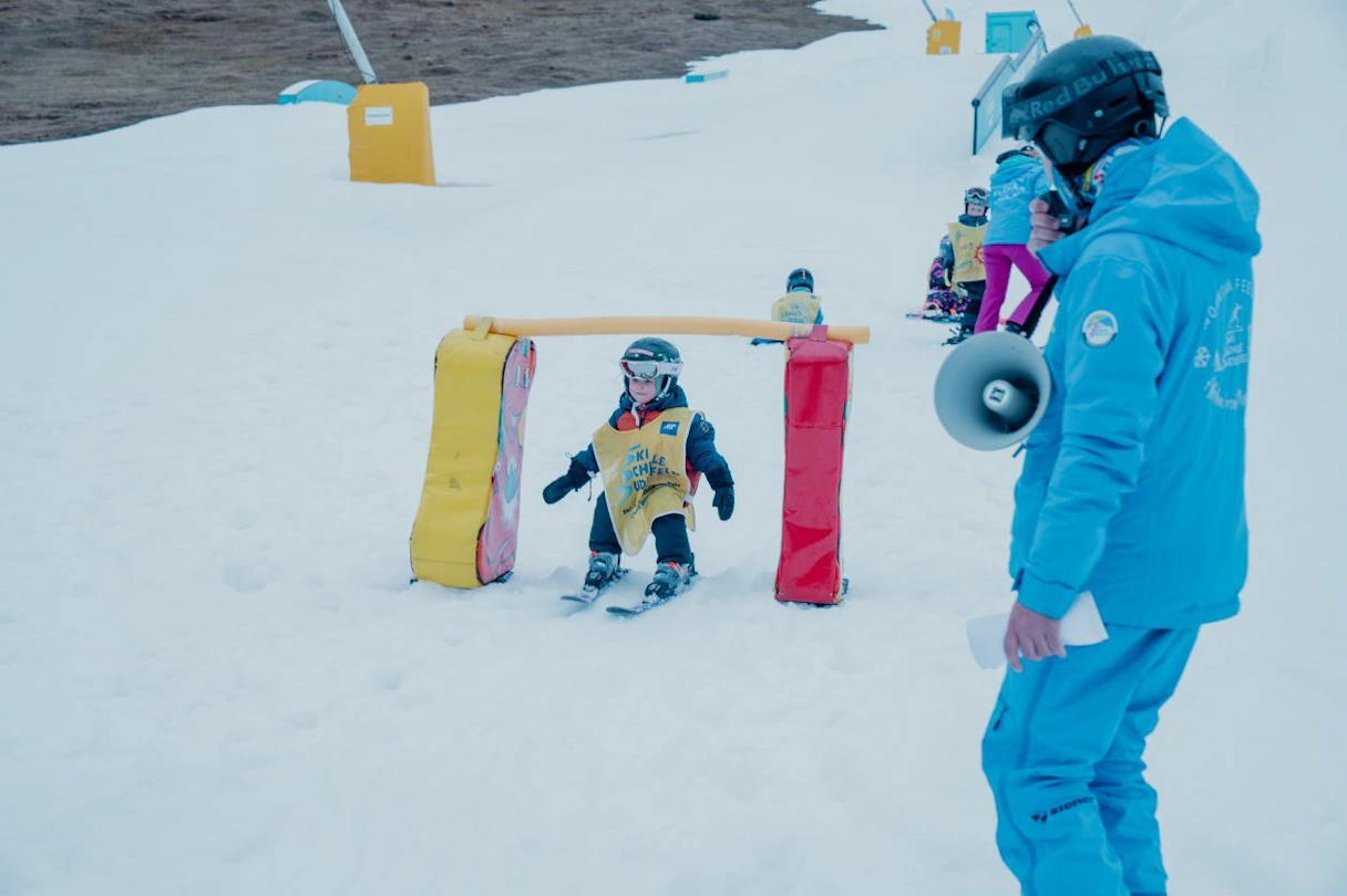 Ski instructor with megaphone. Small child skiing under a hurdle