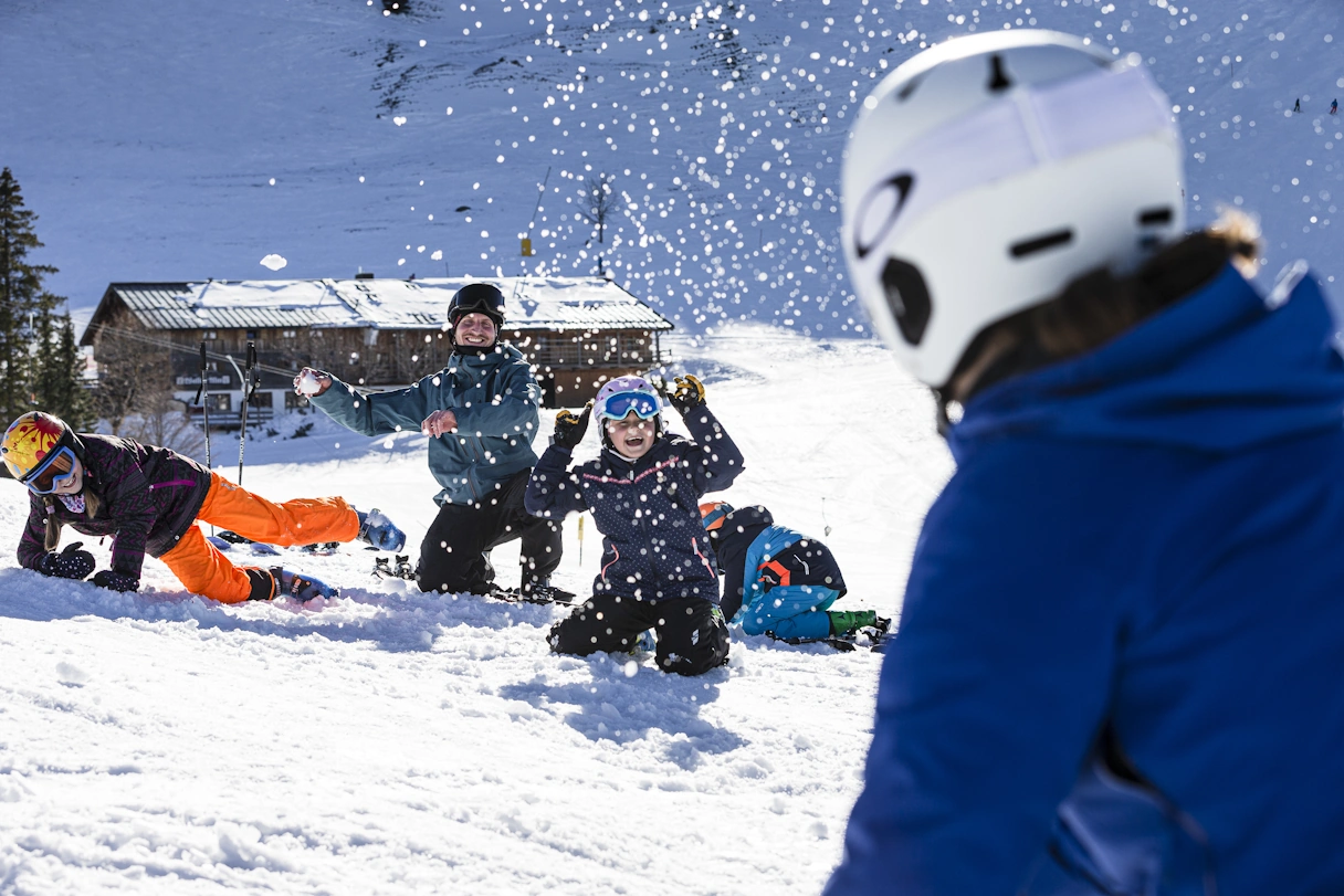 Zwei Kinder und zwei Erwachsene spielen im Schnee und tragen Skikleidung