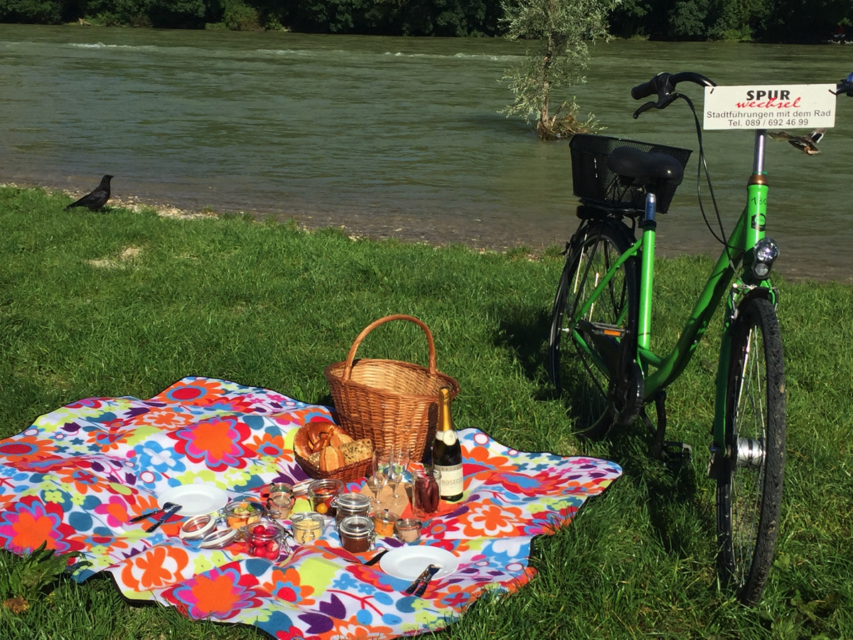 Spurwechsel Fahrradverleih, bike rental, green bike stands next to a colorful picnic blanket on which is a woven basket and all kinds of food